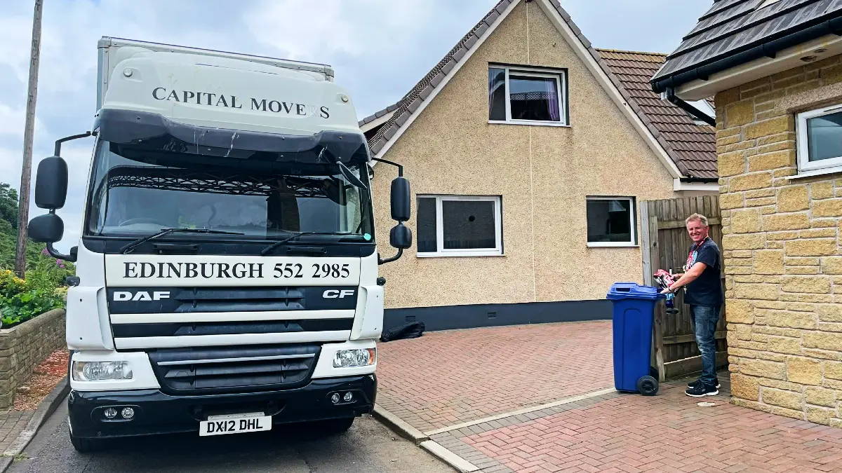 A Capital Mover customer standing proudly next to the branded truck in a driveway, showcasing customer satisfaction of Capital Movers services.