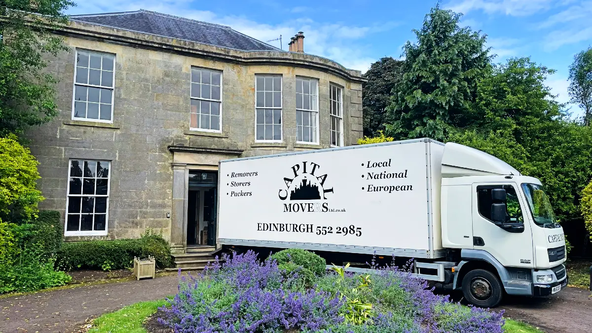 Capital Movers white removal lorry positioned at the entrance of a traditional Edinburgh stone house with garden and blue door, demonstrating careful residential access.